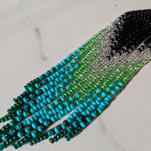Load image into Gallery viewer, A close-up of a beaded fringe earrings, strands transition from black at one end through clear and green beads to bright turquoise and dark teal at the other.
